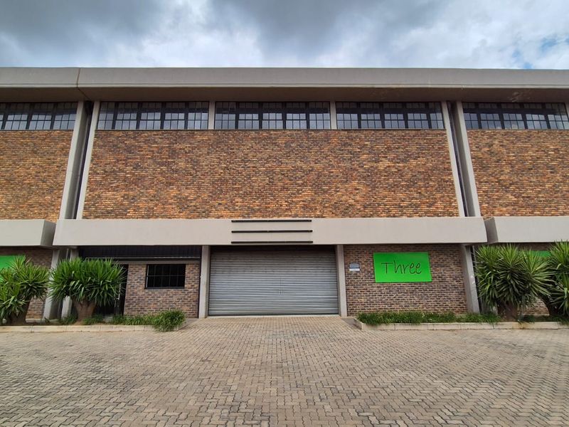 Front elevation of an industrial warehouse building featuring a brick facade, large roller shutter door, and clerestory windows above a paved driveway.
