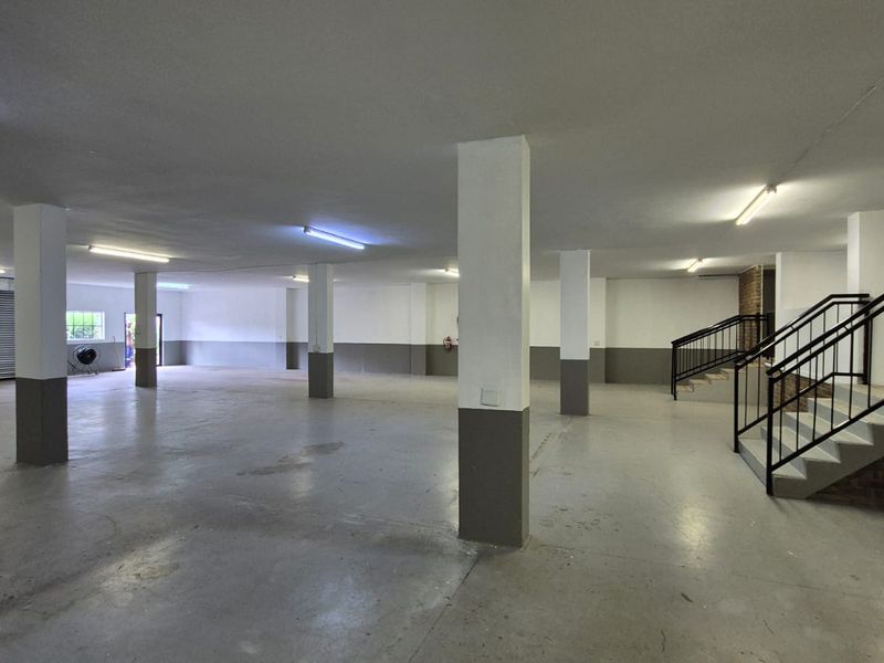 Spacious industrial utility area featuring concrete flooring, structural columns, fluorescent lighting, and a staircase with metal railings.