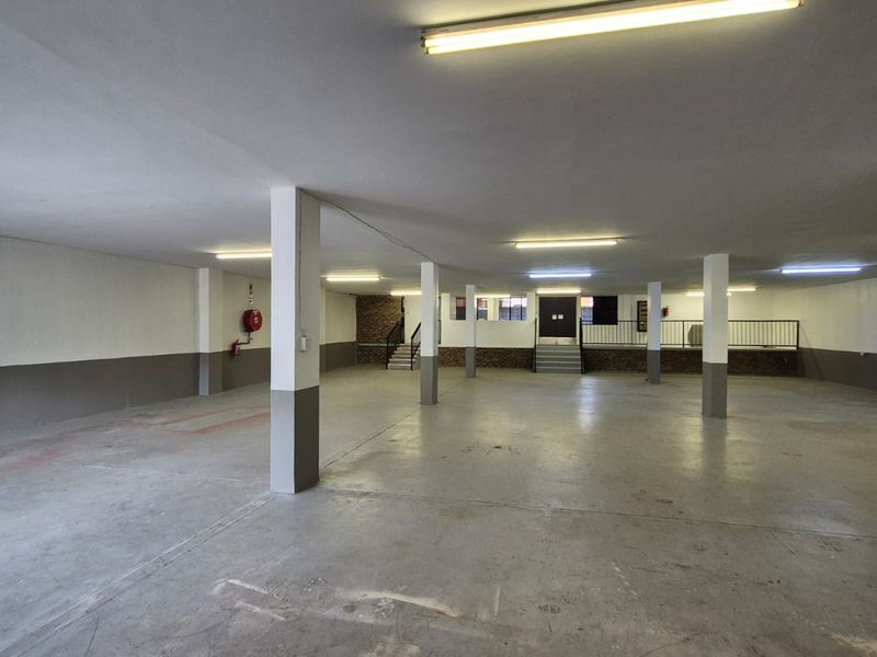 A spacious, open-plan industrial garage or storage area featuring concrete flooring, structural support columns, and functional overhead fluorescent lighting.