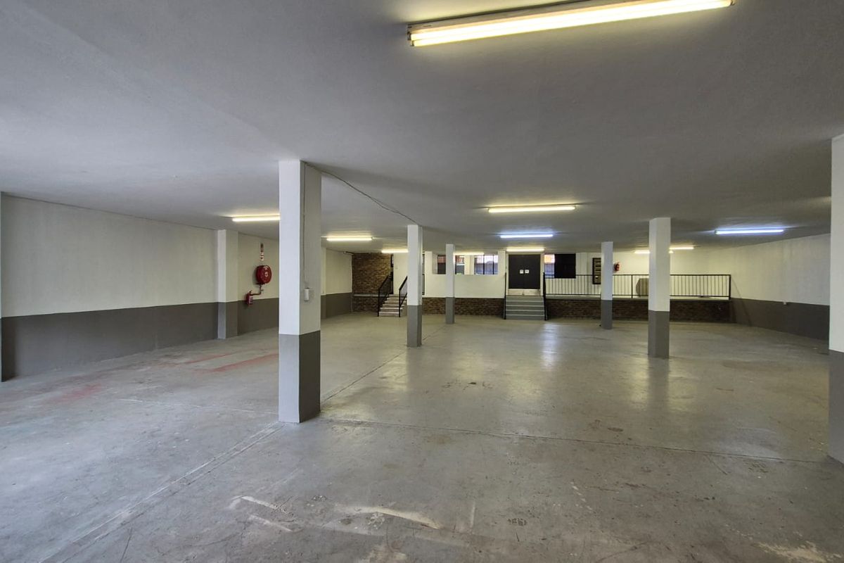 A spacious, open-plan industrial garage or storage area featuring concrete flooring, structural support columns, and functional overhead fluorescent lighting.