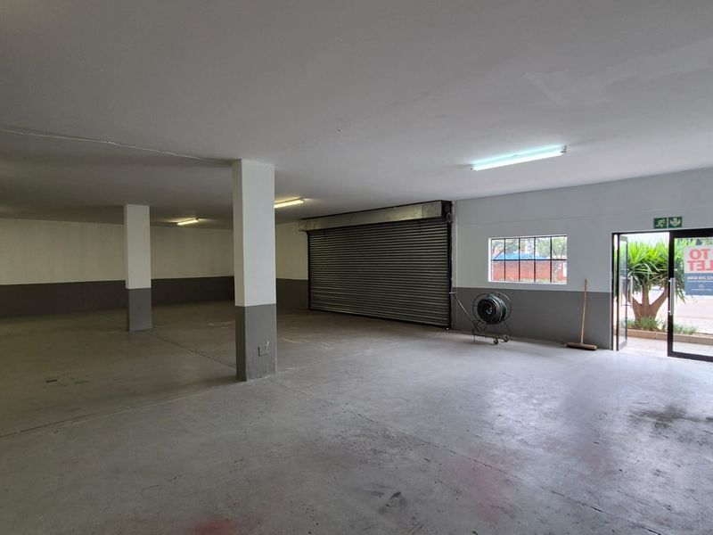 Spacious industrial garage or warehouse area featuring concrete flooring, structural support columns, a large roller shutter door, and direct exterior access.