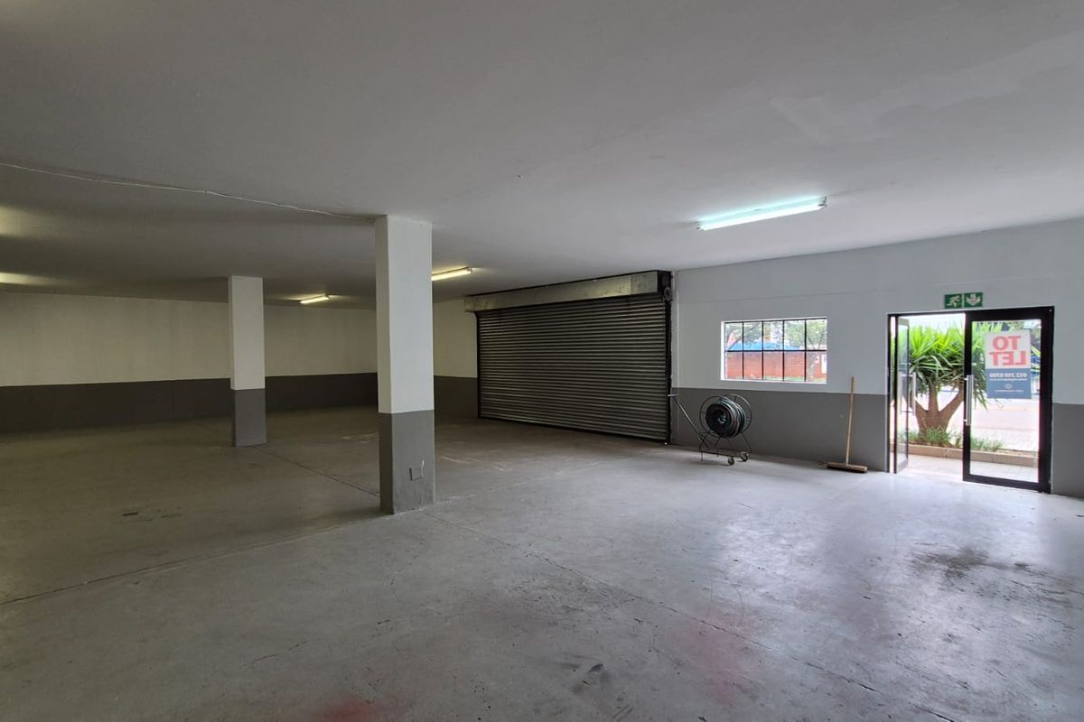 Spacious industrial garage or warehouse area featuring concrete flooring, structural support columns, a large roller shutter door, and direct exterior access.