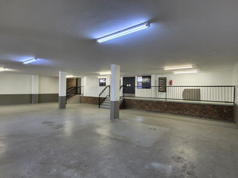 Spacious industrial garage area featuring concrete flooring, fluorescent lighting, and a raised platform with metal railings and brick detailing.