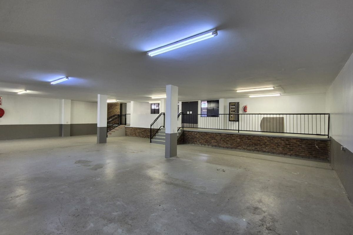 Spacious industrial garage area featuring concrete flooring, fluorescent lighting, and a raised platform with metal railings and brick detailing.