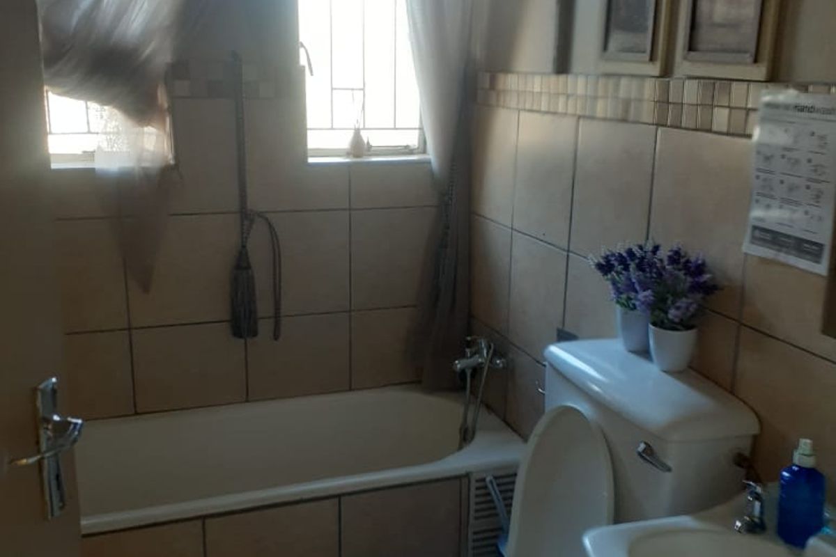A functional bathroom featuring a bathtub, toilet, and washbasin with tiled finishes and security bars on the windows.