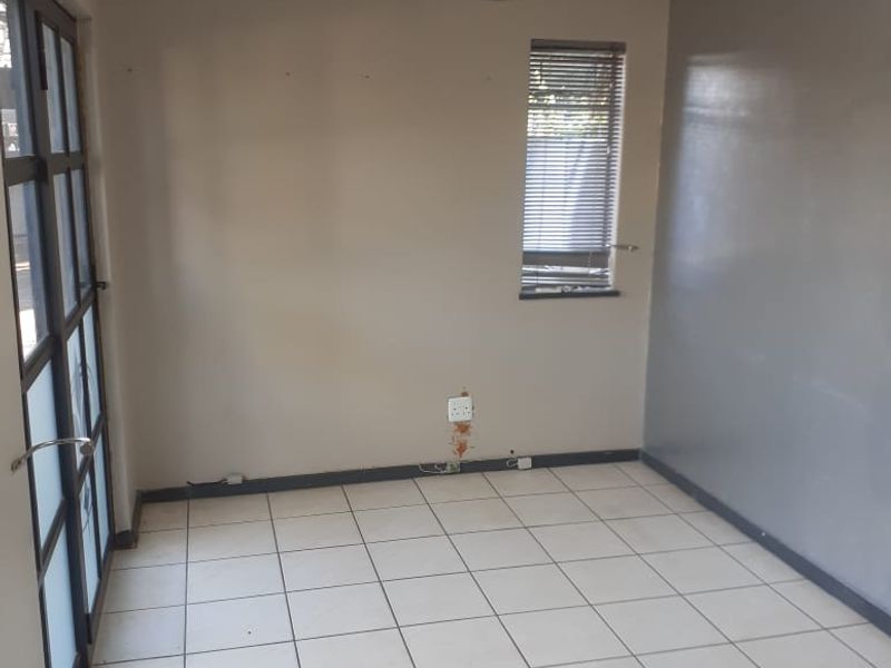 A vacant office space featuring tiled flooring, a split-system air conditioner, and large glass-panelled doors providing natural light.