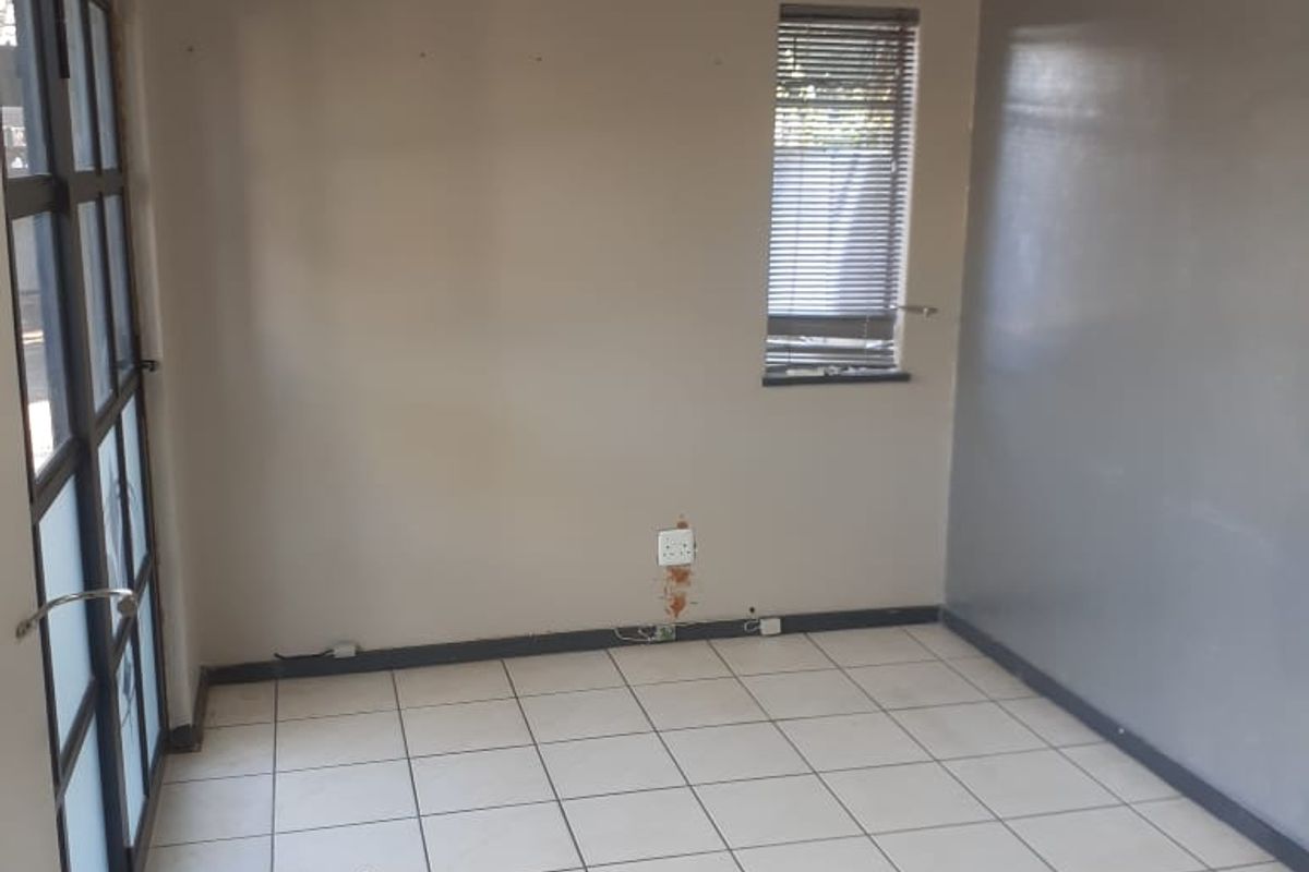 A vacant office space featuring tiled flooring, a split-system air conditioner, and large glass-panelled doors providing natural light.