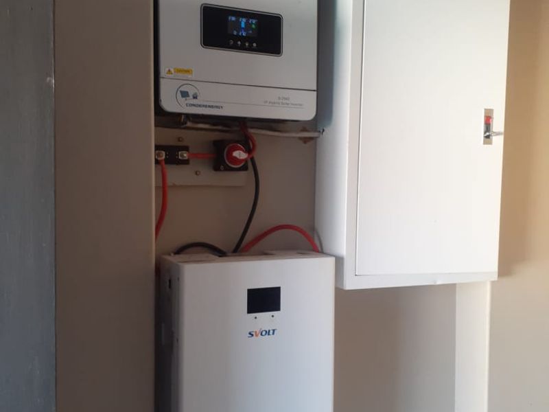 A clean utility area featuring a wall-mounted solar inverter, lithium battery storage system, and an electrical distribution board.