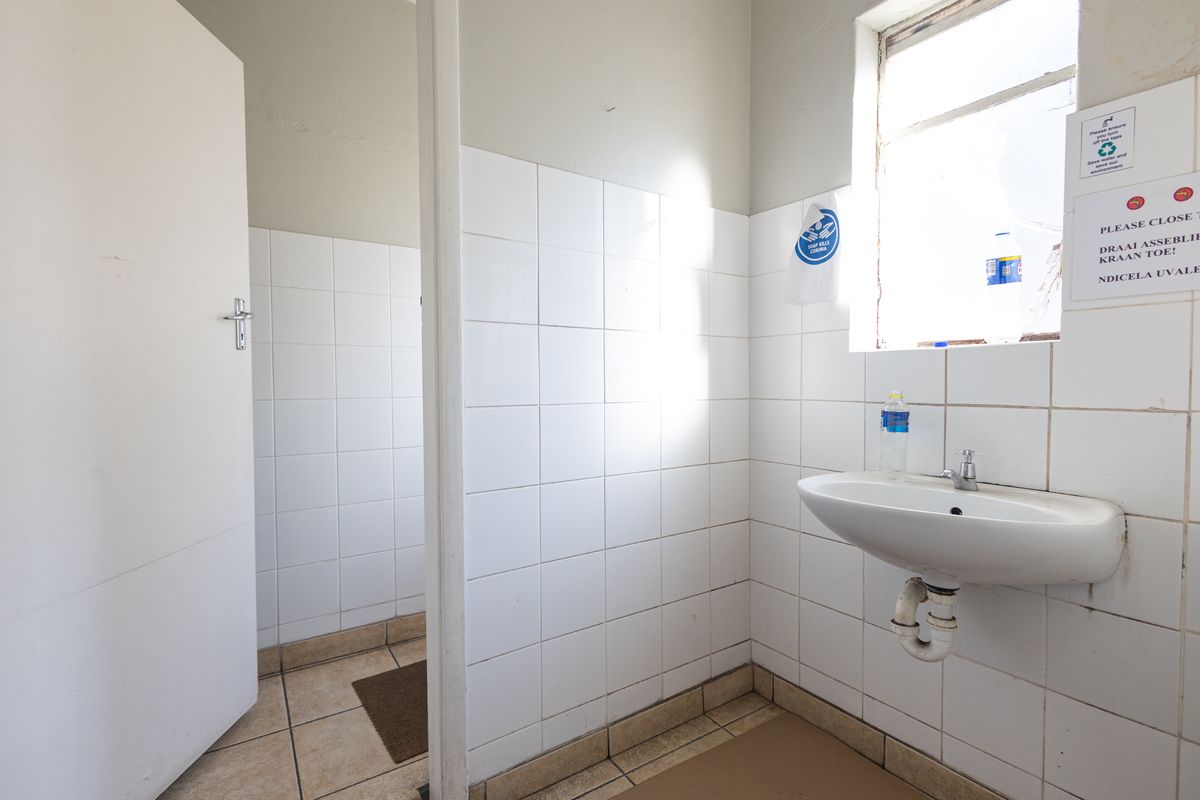 A functional industrial-style bathroom featuring a wall-mounted basin, tiled walls, and tiled flooring, requiring minor maintenance and cosmetic updates.
