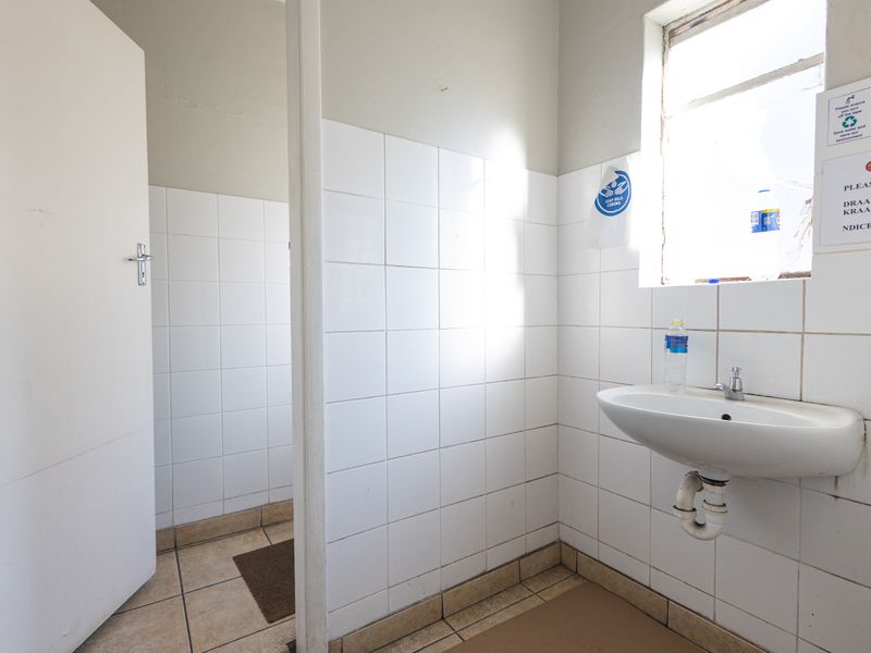 A functional industrial-style bathroom featuring a wall-mounted basin, tiled walls, and tiled flooring, requiring minor maintenance and cosmetic updates.