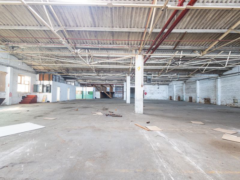 Expansive industrial warehouse space featuring high ceilings with exposed steel trusses, concrete flooring, and brick walls, suitable for various commercial or storage applications.