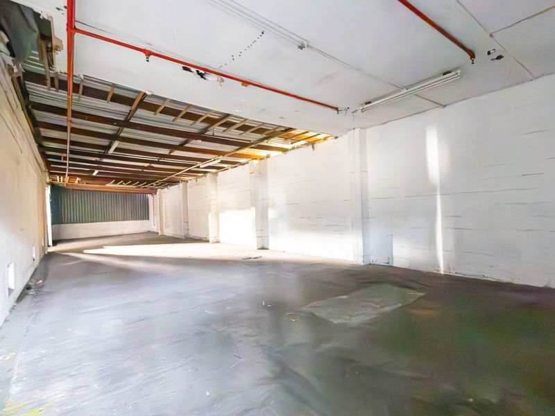 An expansive, open-plan industrial utility space featuring exposed ceiling infrastructure, fire sprinkler piping, and painted masonry walls with concrete flooring.