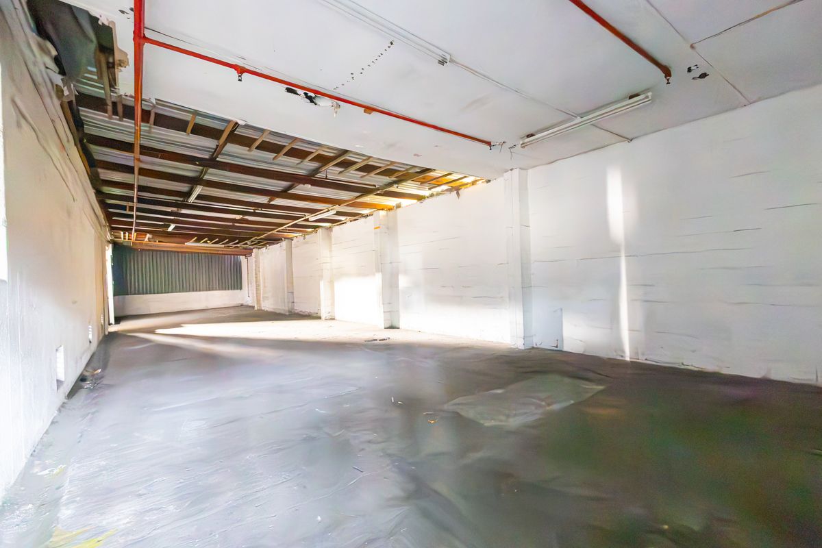An expansive, open-plan industrial utility space featuring exposed ceiling infrastructure, fire sprinkler piping, and painted masonry walls with concrete flooring.