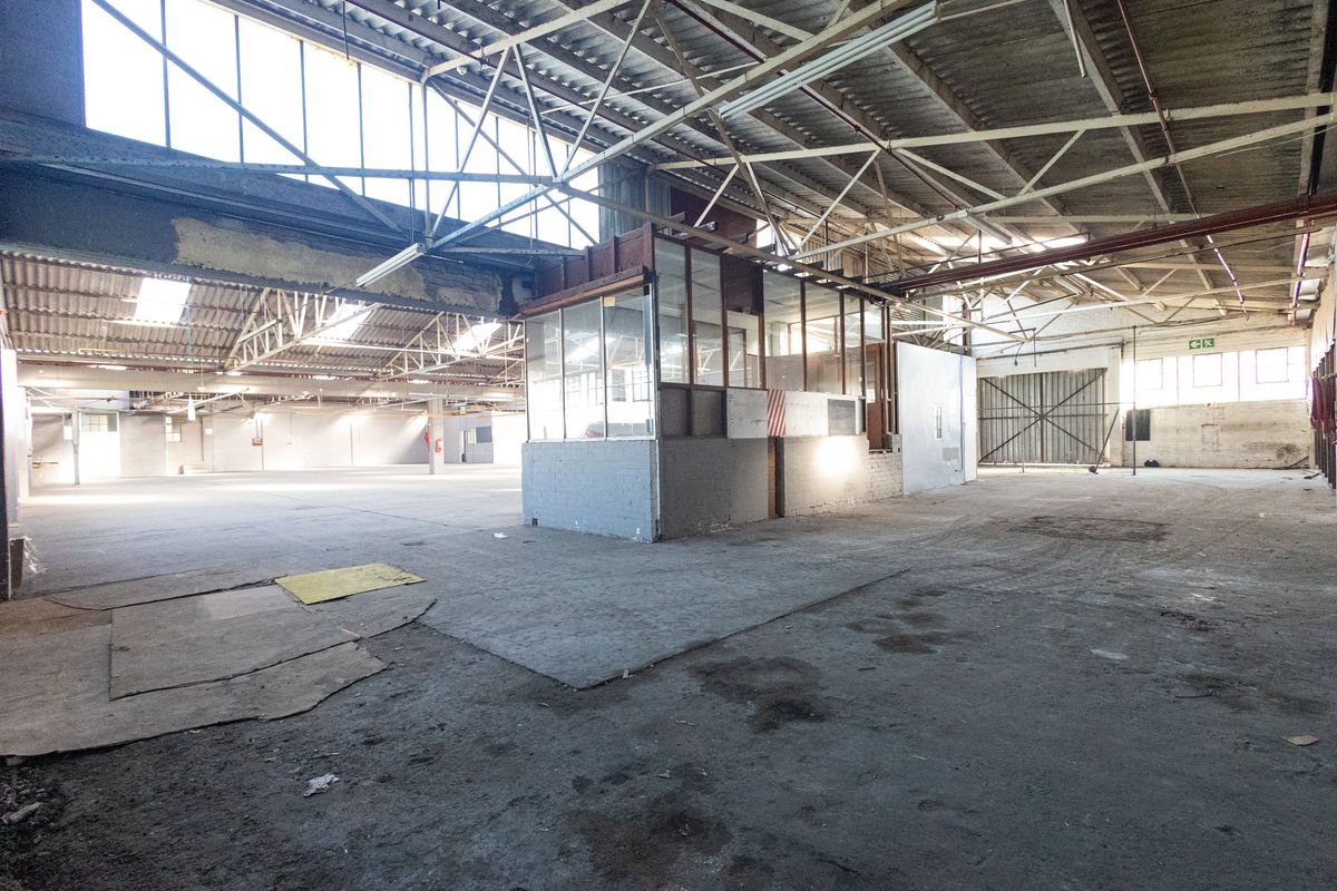 Spacious industrial warehouse featuring high exposed steel roof trusses, concrete flooring, and an internal office enclosure, suitable for various commercial or storage applications.