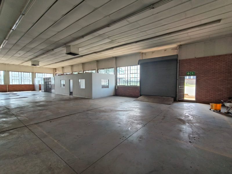 Spacious industrial warehouse featuring high ceilings, concrete flooring, a large roller shutter door, and an internal partitioned office area.