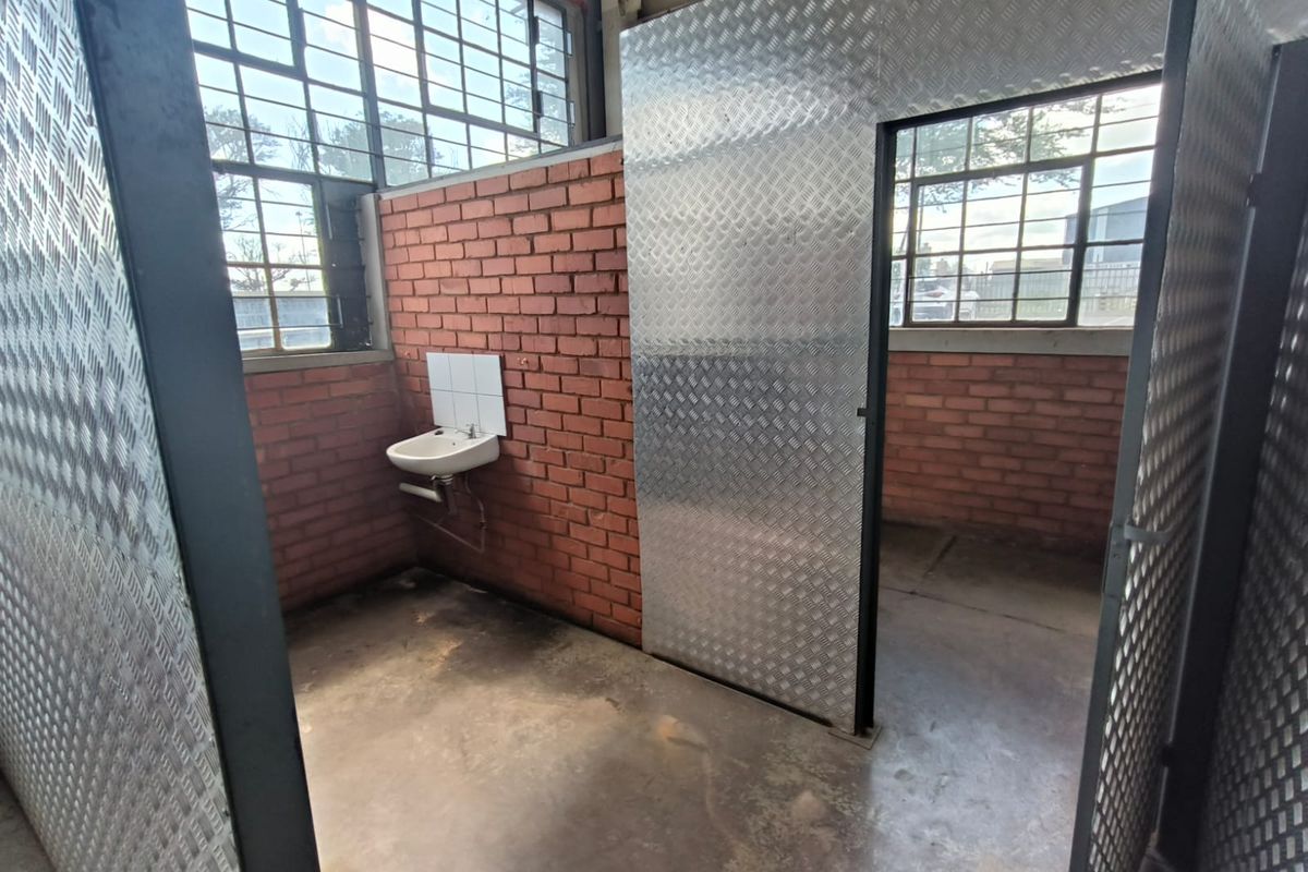 Industrial-style bathroom facility featuring exposed brick walls, checker plate metal partitions, concrete flooring, and large steel-framed windows.