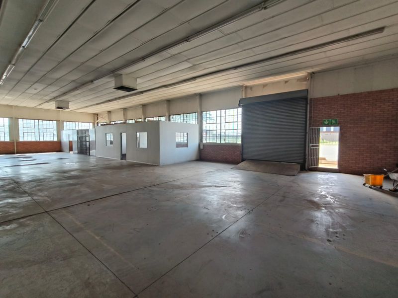 Spacious industrial warehouse featuring concrete flooring, high ceilings with exposed steel structure, roller shutter door access, and an internal office partition.
