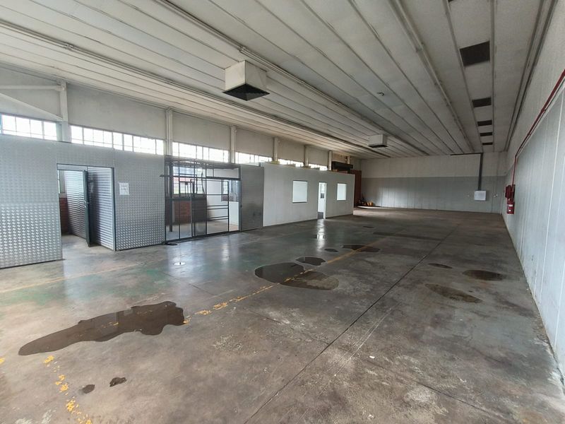Spacious industrial warehouse area featuring concrete flooring, high metal ceilings, and partitioned office sections, suitable for various commercial or storage applications.