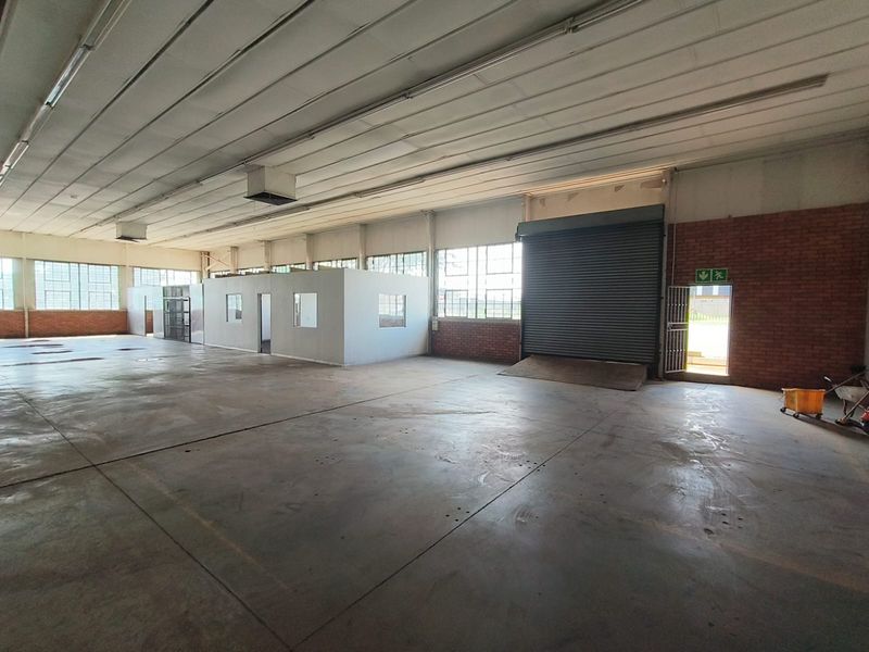 Spacious industrial warehouse featuring concrete flooring, high ceilings with exposed structure, internal office partitioning, and a large roller shutter door for loading access.