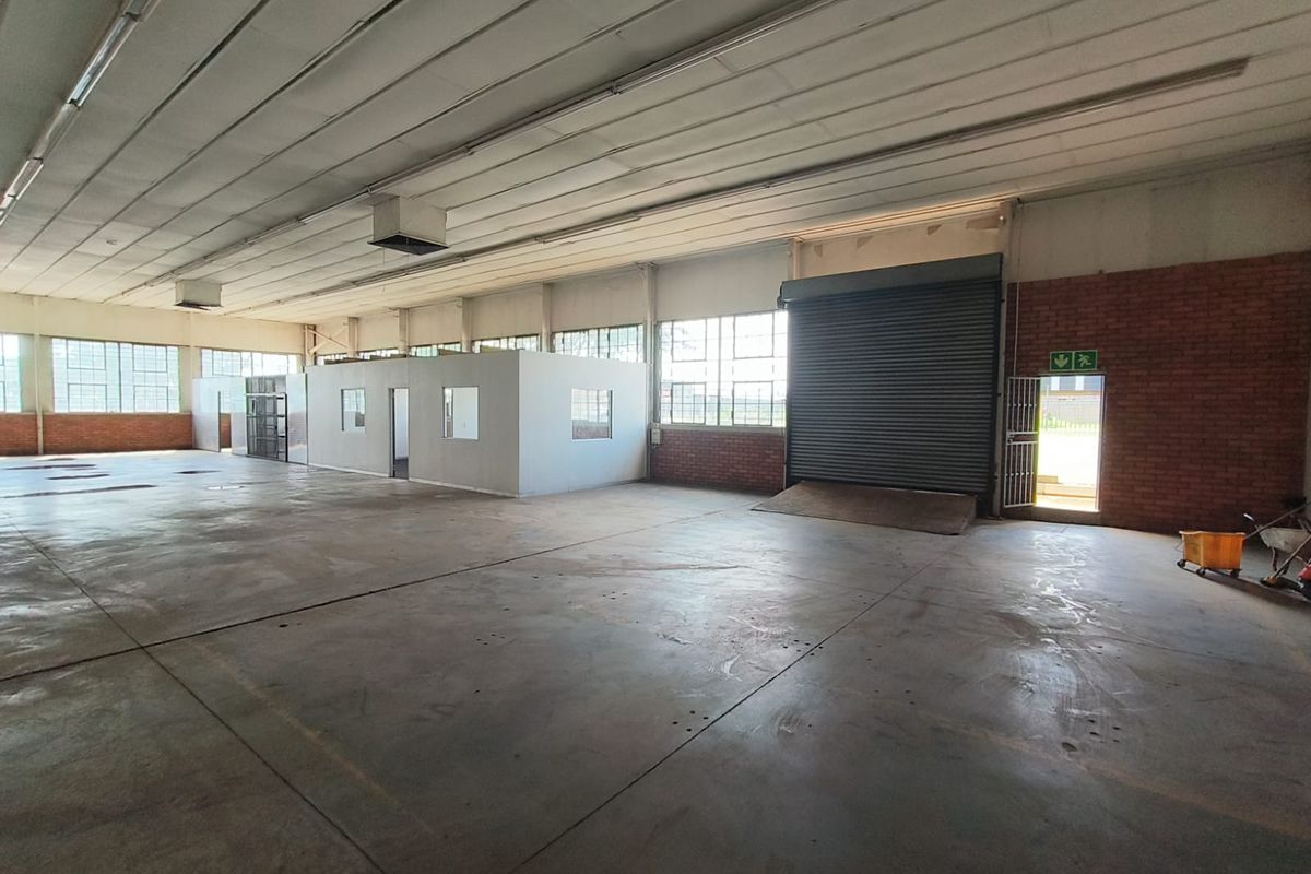 Spacious industrial warehouse featuring concrete flooring, high ceilings with exposed structure, internal office partitioning, and a large roller shutter door for loading access.