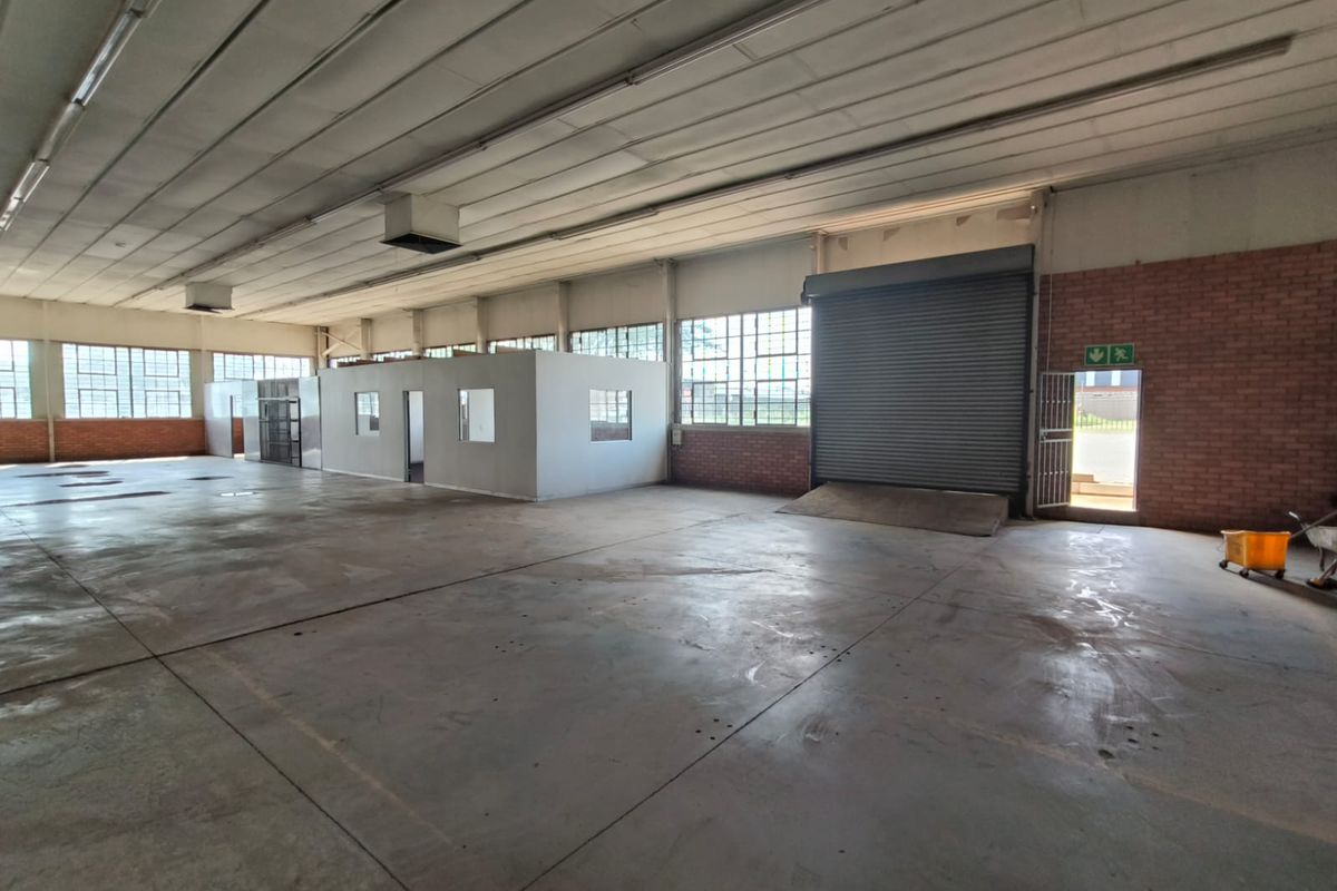 Spacious industrial warehouse featuring concrete flooring, high ceilings with exposed steel structure, roller shutter door access, and an internal office partition.