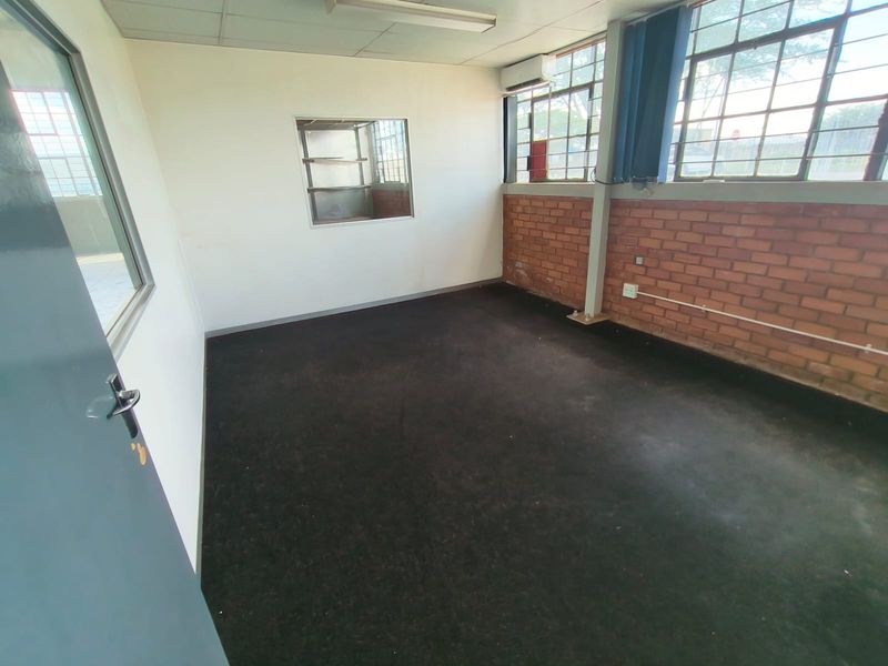 An empty office space featuring exposed brick walls, steel-framed windows, air conditioning, and carpeted flooring, suitable for a professional workspace.