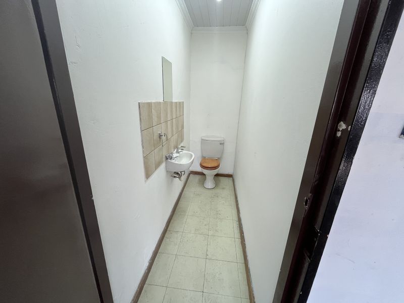 A compact, functional bathroom featuring a wall-mounted basin with tiled splashback and a standard toilet, finished with tiled flooring.