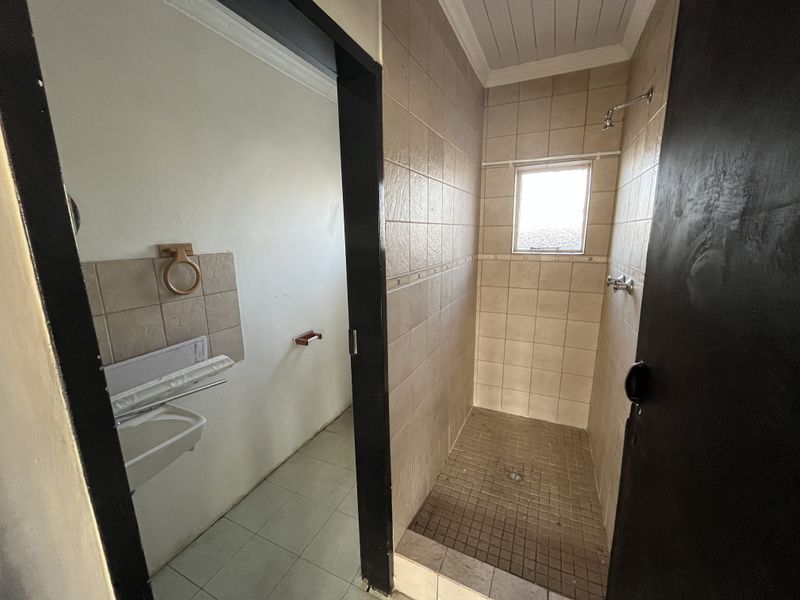 A functional bathroom featuring a tiled shower enclosure and a wall-mounted basin, presenting an opportunity for modernization and cosmetic updates.