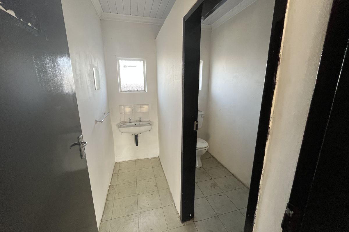 A functional, empty bathroom featuring a wall-mounted basin, toilet, and tiled flooring, requiring cosmetic updates to improve its overall condition.