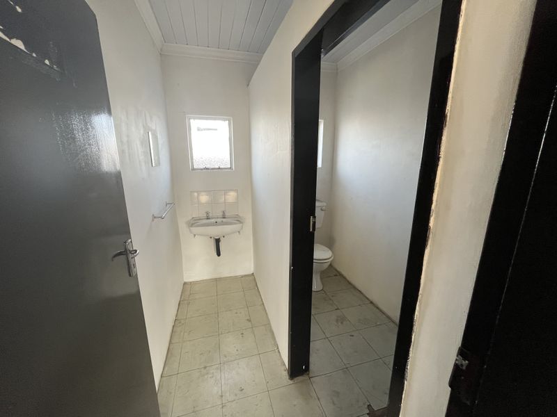 A functional, empty bathroom featuring a wall-mounted basin, toilet, and tiled flooring, requiring cosmetic updates to improve its overall condition.