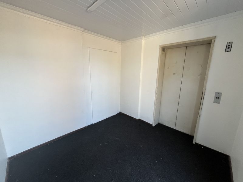 A vacant hallway area featuring a functional elevator, tongue and groove ceiling, and dark carpet flooring in need of maintenance.