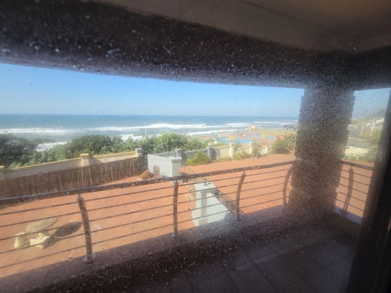 A view from an interior space looking out over a balcony towards the ocean and a swimming pool area.