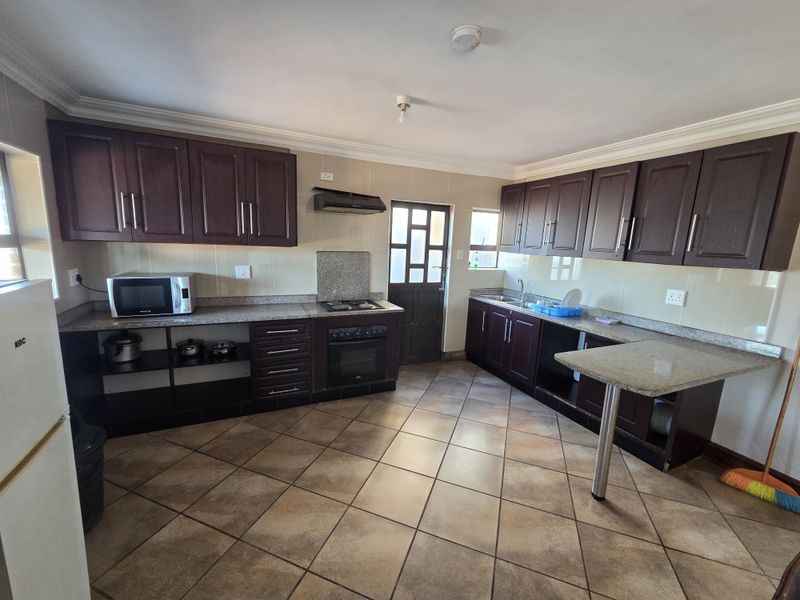 A functional kitchen featuring dark wood cabinetry, granite countertops, built-in oven and hob, and tiled flooring with a breakfast nook area.