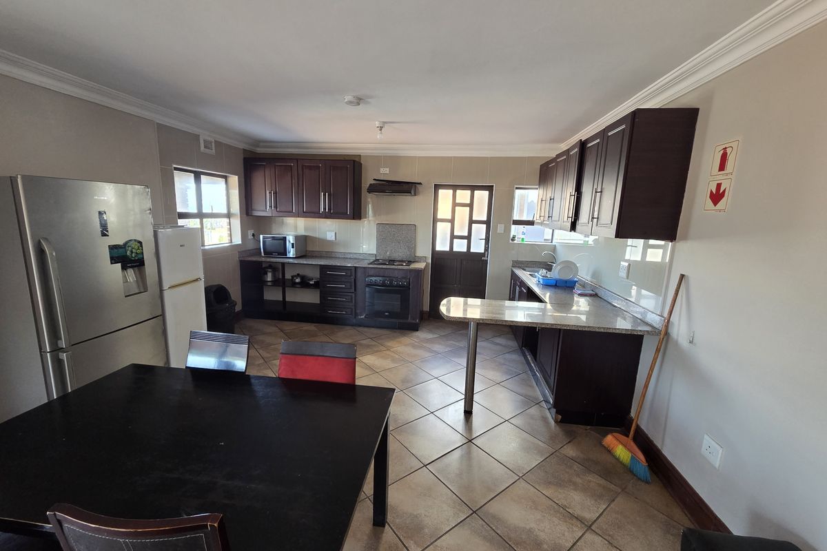 Functional kitchen featuring dark wood cabinetry, granite countertops, built-in oven, hob, and extractor fan, with tiled flooring and direct exterior access.