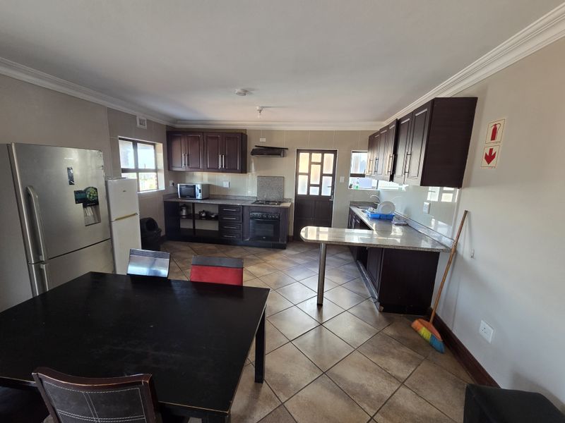 Functional kitchen featuring dark wood cabinetry, granite countertops, built-in oven, hob, and extractor fan, with tiled flooring and direct exterior access.