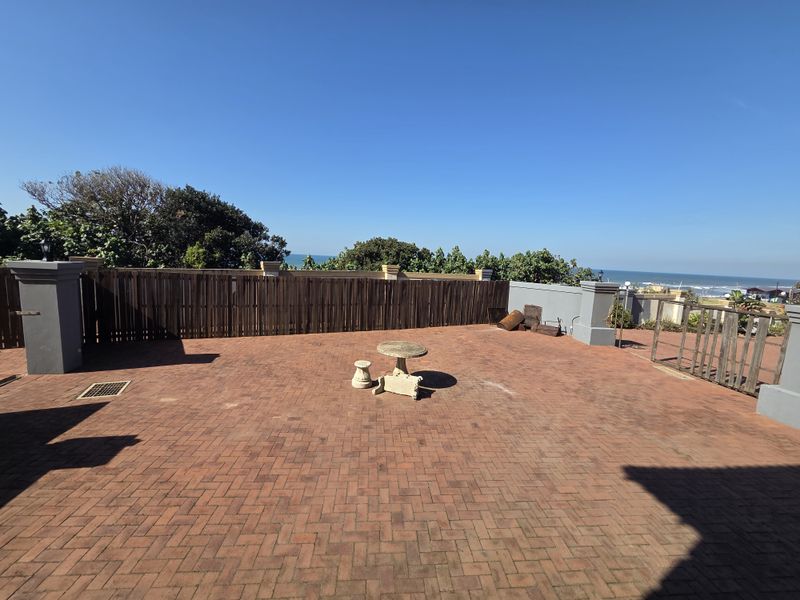 Spacious outdoor patio area featuring brick paving, masonry pillars, and timber fencing with ocean views.