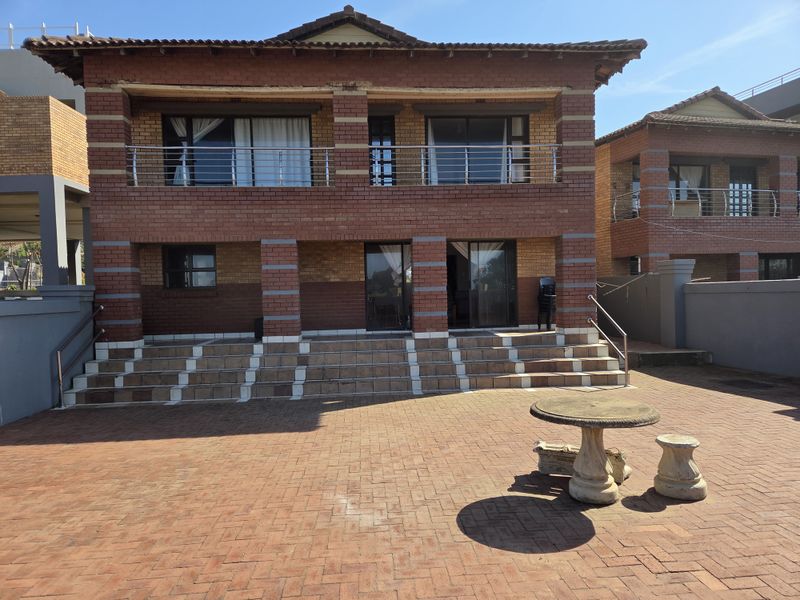 Rear view of a two-story brick office building featuring a paved patio area, balcony with stainless steel railings, and sliding glass door access.