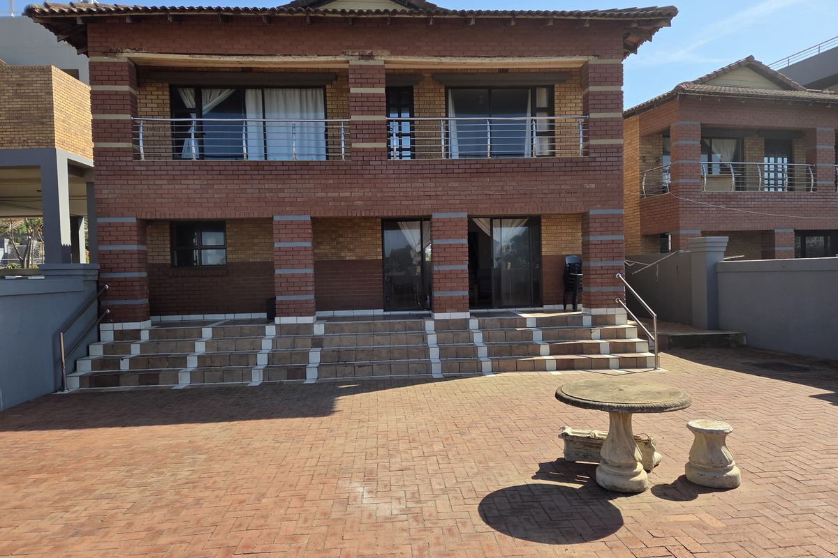 Rear view of a two-story brick office building featuring a paved patio area, balcony with stainless steel railings, and sliding glass door access.