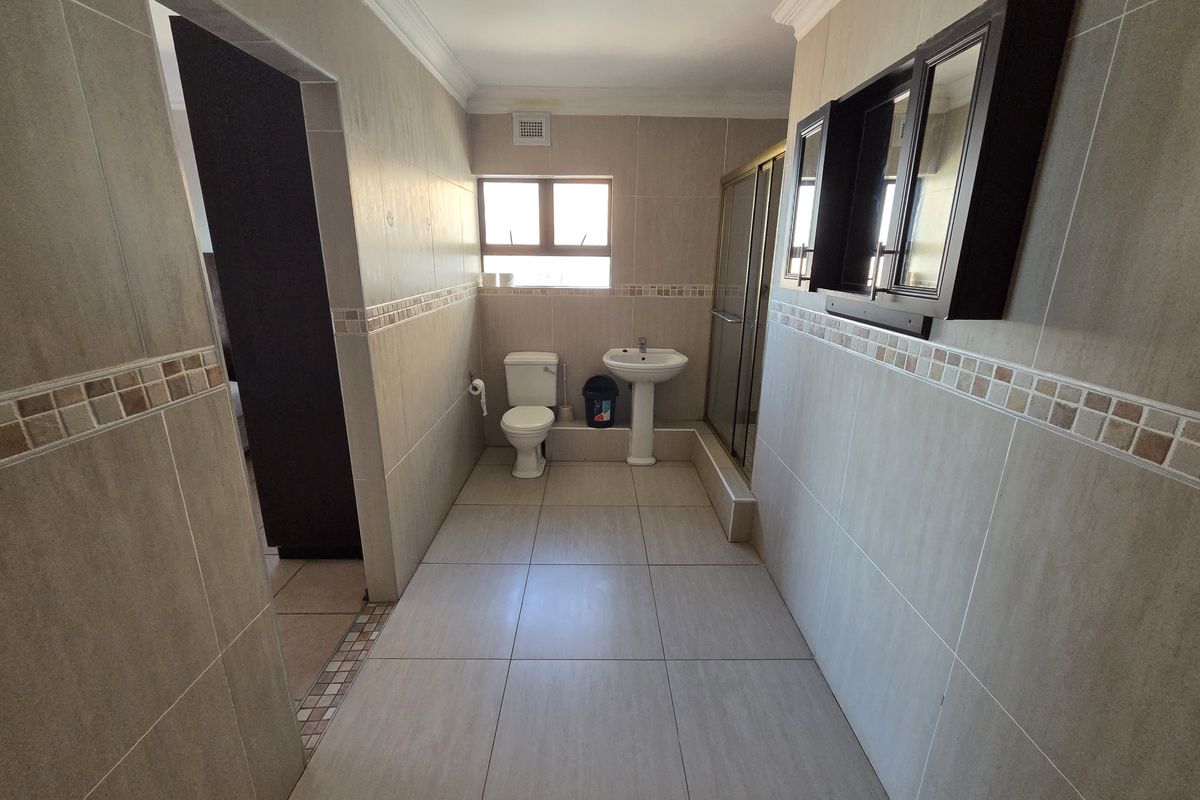 A well-maintained bathroom featuring tiled walls and flooring, a pedestal basin, a toilet, and a glass-enclosed shower.