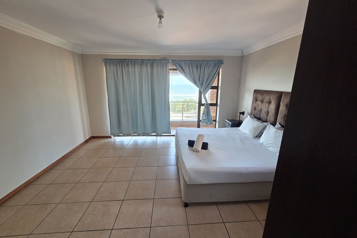 Spacious bedroom featuring tiled flooring, neutral walls, and a sliding glass door providing direct access to a balcony with ocean views.