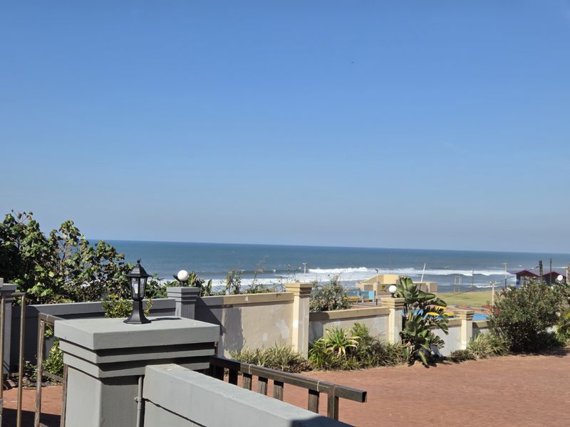 An elevated outdoor terrace area featuring a masonry boundary wall with pillar lighting, offering expansive views of the ocean and coastline.