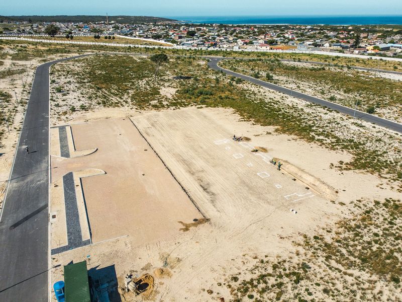 Aerial view of a vacant commercial land plot featuring paved road access, cleared terrain, and site survey markings.