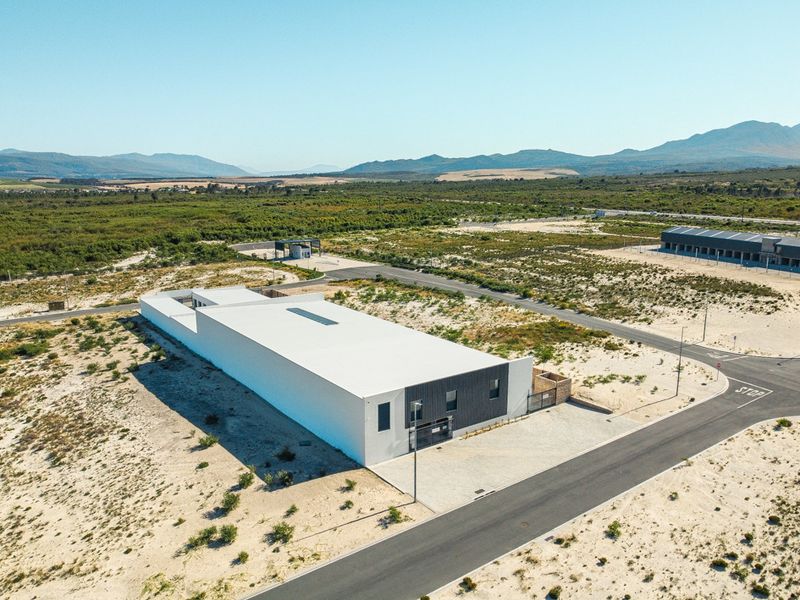 Aerial view of a modern commercial property situated on a large plot with paved access roads and surrounding natural landscape.