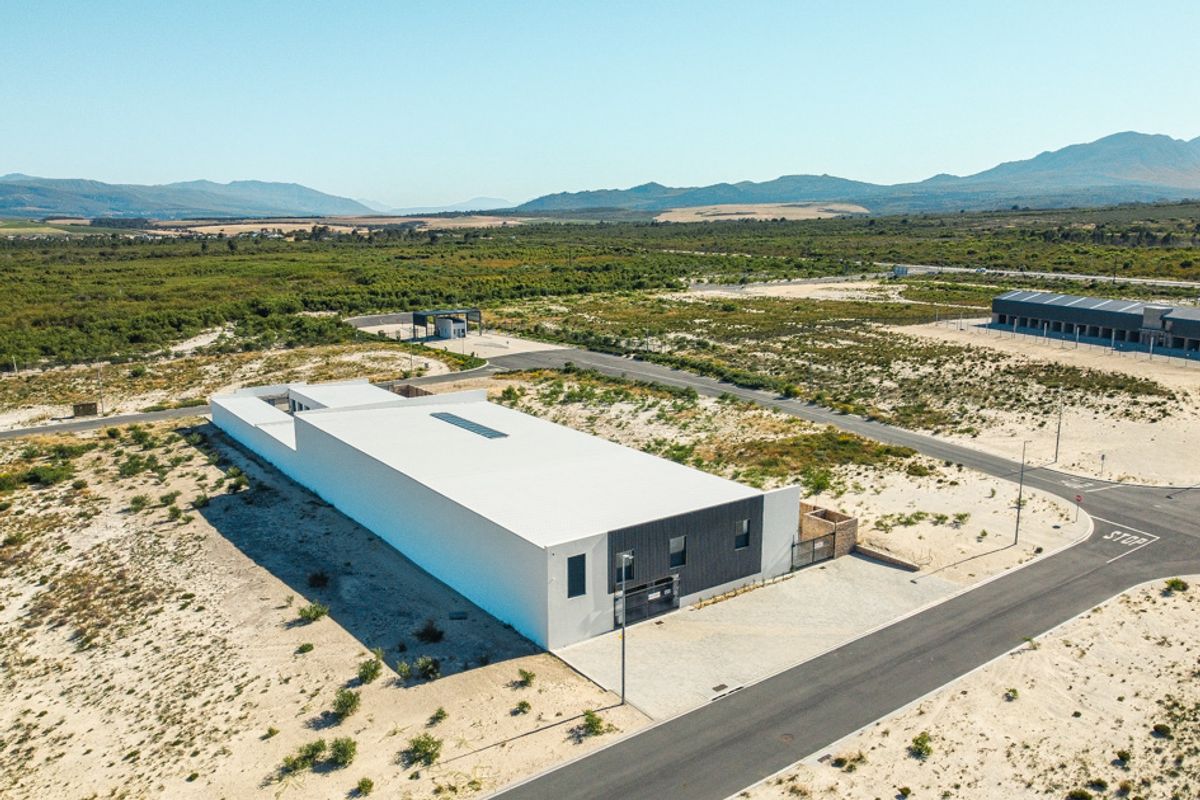 Aerial view of a modern commercial property situated on a large plot with paved access roads and surrounding natural landscape.