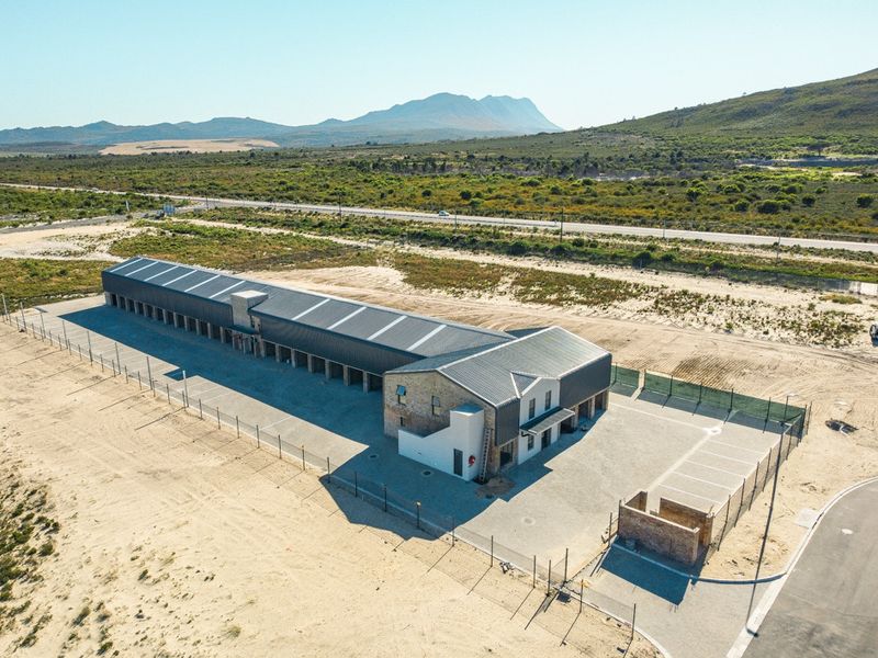 Aerial view of a commercial property featuring a long storage facility with metal roofing, paved parking, and perimeter fencing in a rural landscape.