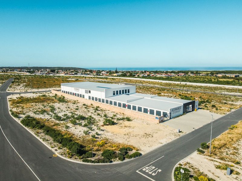 Aerial view of a modern commercial storage facility situated on a large plot with paved road access and coastal views.