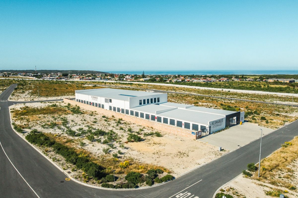 Aerial view of a modern commercial storage facility situated on a large plot with paved road access and coastal views.