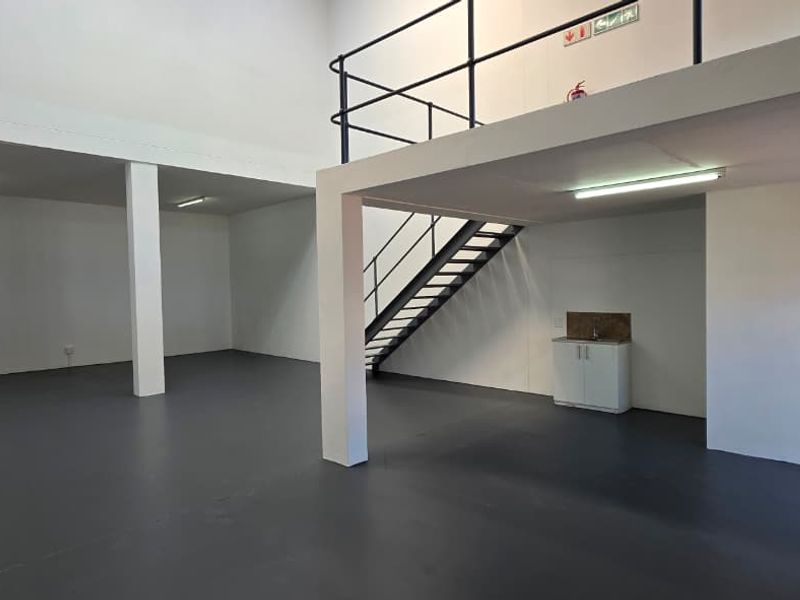 Spacious industrial open-plan unit featuring a mezzanine level, metal staircase, kitchenette area, and durable epoxy flooring, suitable for various commercial or storage uses.