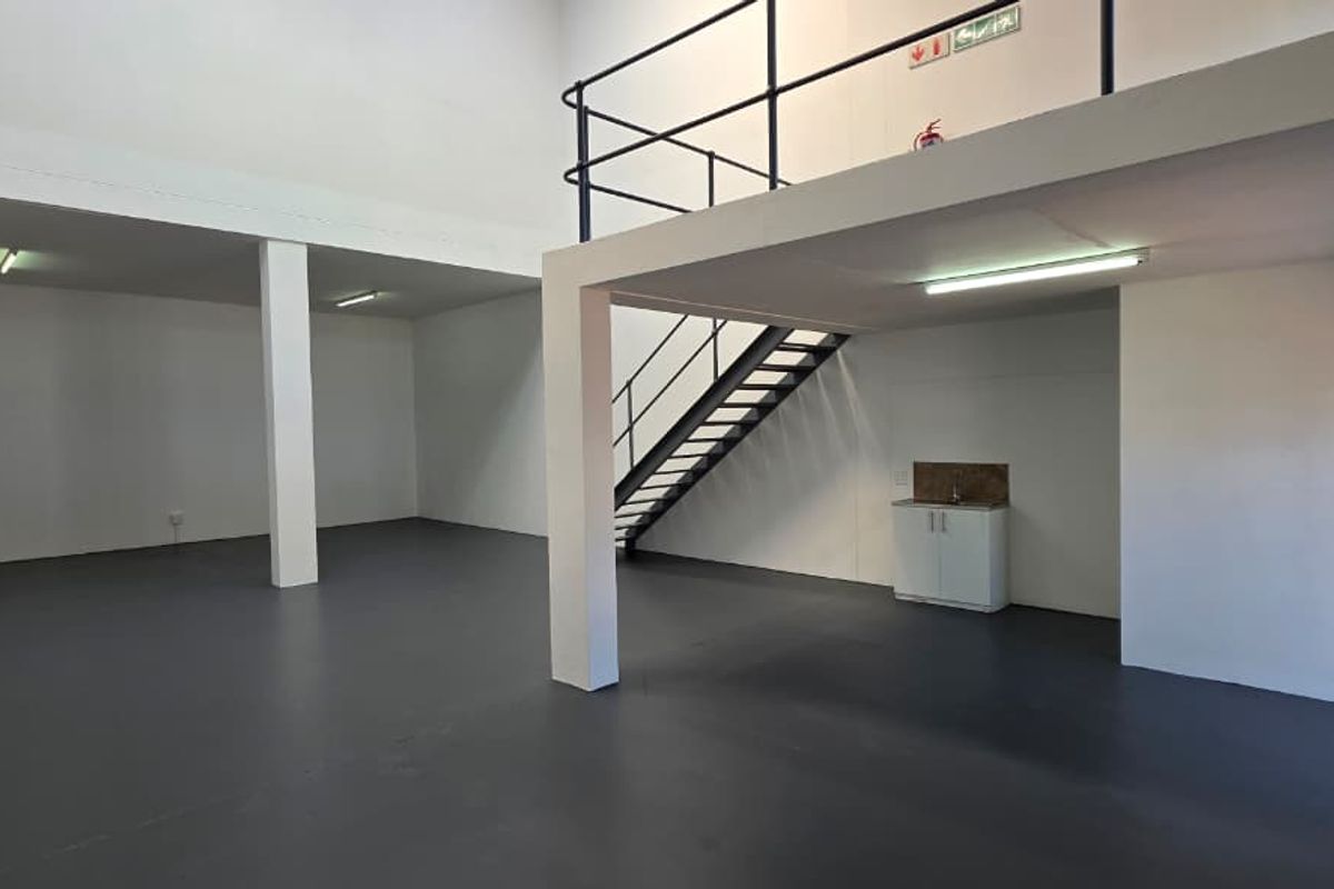 Spacious industrial open-plan unit featuring a mezzanine level, metal staircase, kitchenette area, and durable epoxy flooring, suitable for various commercial or storage uses.