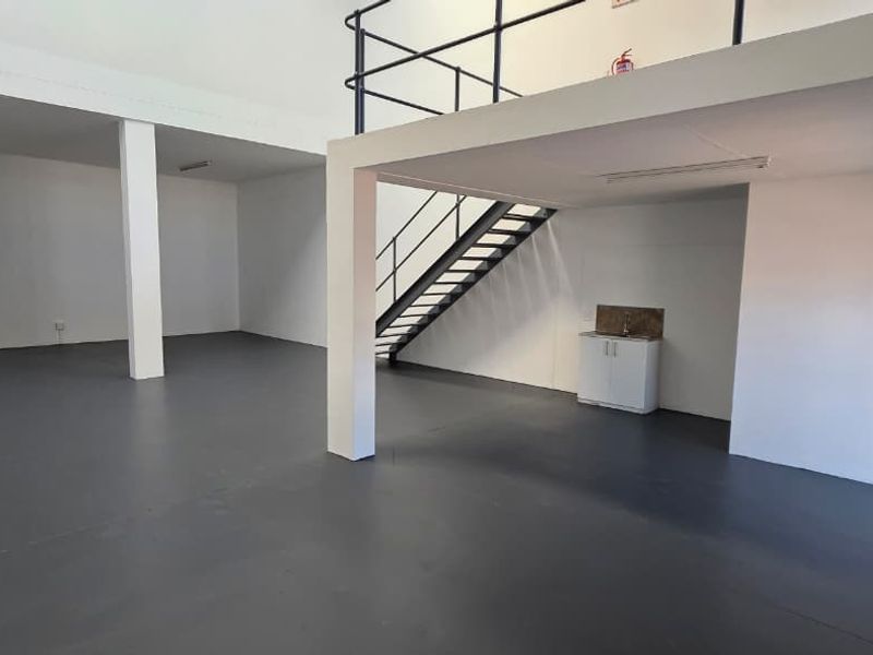 Spacious industrial unit featuring an open-plan ground floor with epoxy flooring, a mezzanine level with safety railing, and a small kitchenette area.